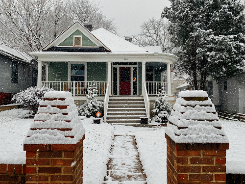 a house covered in snow in front of a brick building