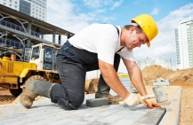 Two construction workers wearing safety vests and hard hats review some documents on a construction site